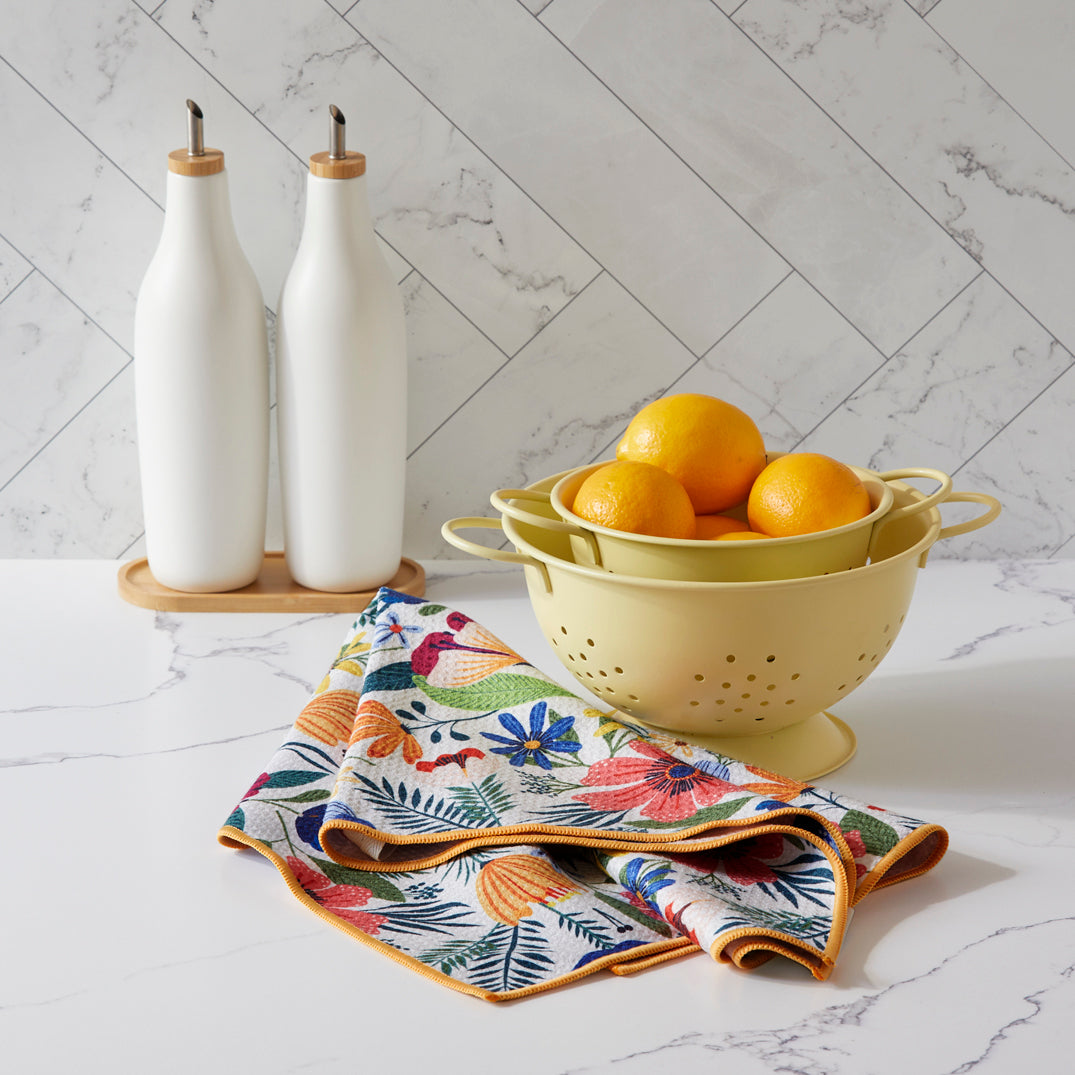 Kitchen scene with a colander, lemons, and floral towels on a marble countertop.