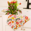 Colorful butterfly and floral patterned tablecloth on a white cabinet with tulips in the background.