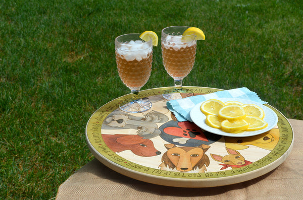 Decorative lazy susan with dog designs, glasses of iced tea, and a plate of lemons on a grassy background.