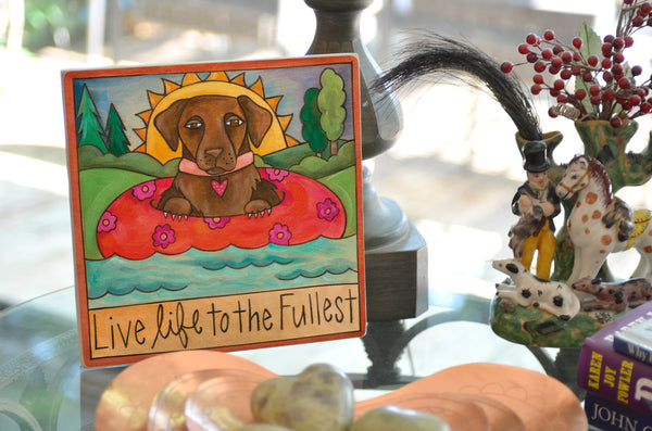 Decorative wall plaque featuring a brown lab in a pink floral inner tube with the words 'Live life to the Fullest' below.