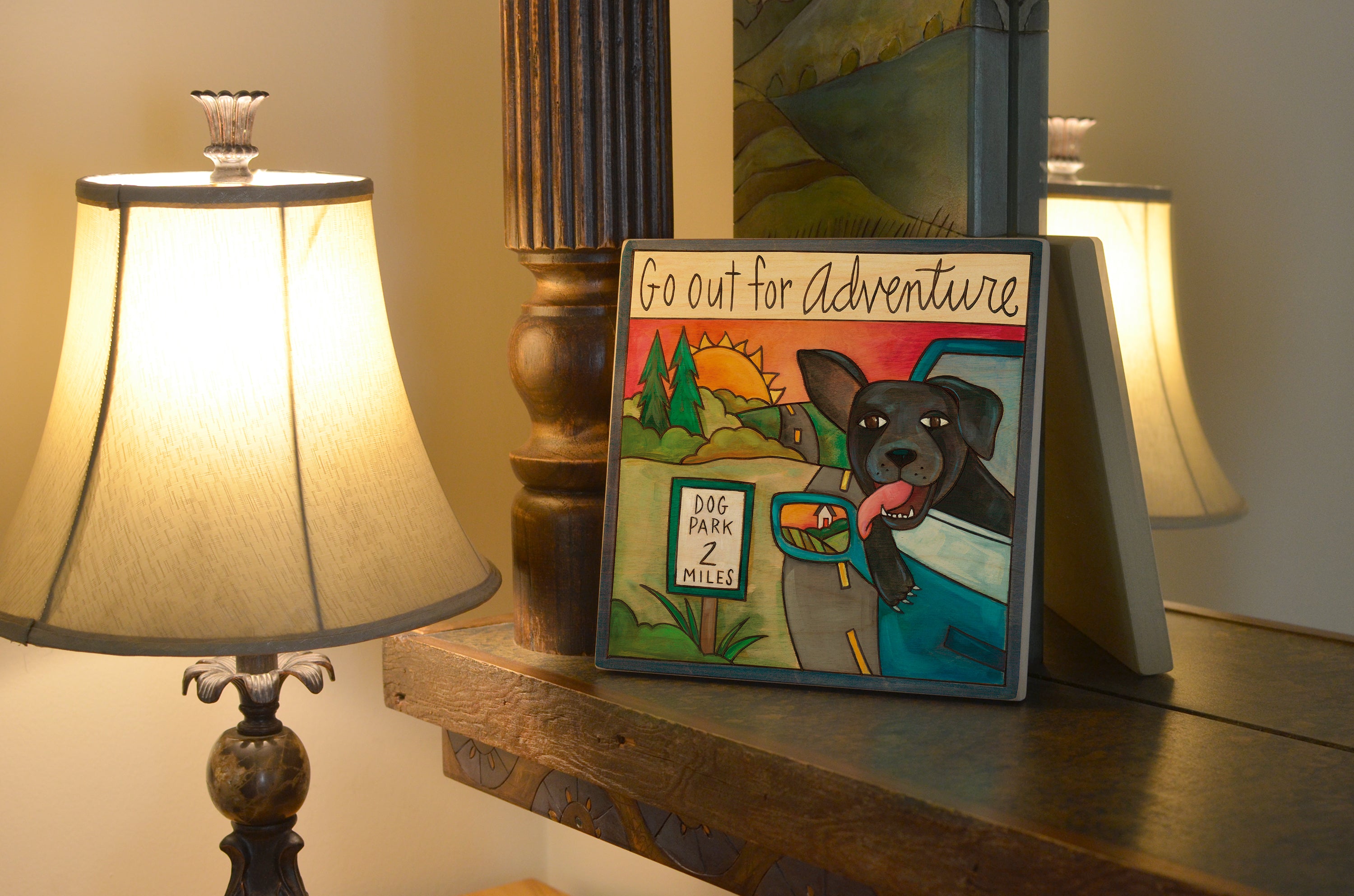 Decorative sign with a dog illustration and text 'Go out for Adventure' on a wooden surface with lamps.