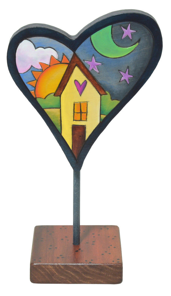 Decorative heart-shaped sculpture with a house design on a stand against a white background