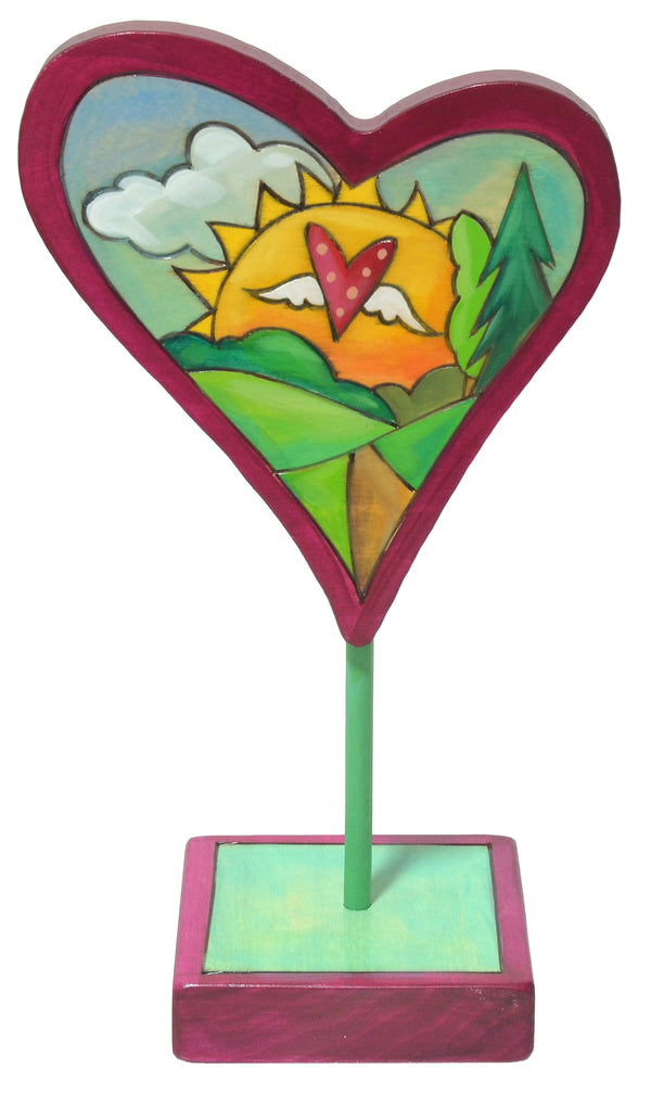Decorative heart-shaped sculpture with a colorful design of a sun and mountains on a white background.