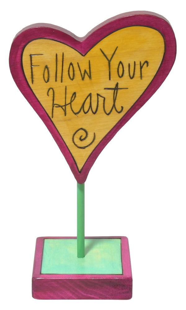 Heart-shaped sculpture with 'Follow Your Heart' text on a stand