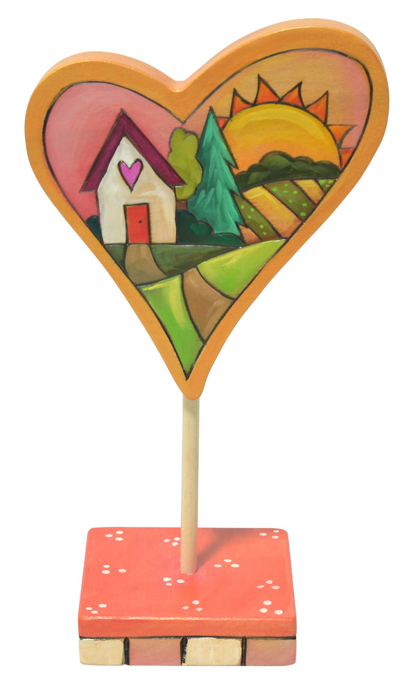 Heart-shaped decorative item with a house, tree, and sun on a white background