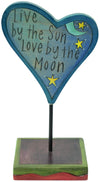 Heart-shaped blue sculpture with 'Live by the Sun, Love by the Moon' text on a stand.