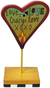 Heart-shaped sculpture with 'Love Crazy Love XOXO' text on a stand