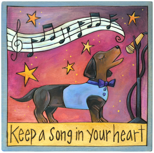 Colorful wood plaque of a Dachshund dog wearing a vest and bowtie, singing with music notes and stars, featuring the text 'Keep a Song in Your Heart'.