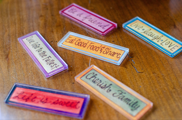 Colorful rectangular acrylic magnets with motivational phrases on a wooden surface