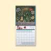 A hanging monthly calendar page with a decorative floral illustration at the top and a May calendar grid below, shown against a pale cream background.