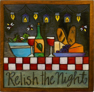 Sticks handmade wall plaque with "Relish the night" quote and outdoor evening dinner with string lights