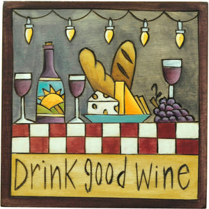 "Drink good wine" plaque with wine and cheese on a patio under string lights