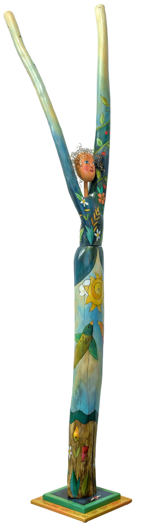 Vibrantly painted with flowers and vines wrapped around the trunk and torso combined with a sky scene. Side view.