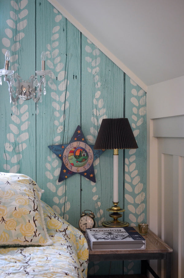 "Who Hung the Moon" Star Clock – A moon and starry sky surround a home nestled into a landscape displayed over a nightstand