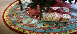 "Run, Run, Rudolph" Tree Skirt – Rudolph and his reindeer crew circle around a starry-sky landscape on our canvas tree skirt displayed under a tree with presents