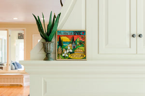 "Where the Trillium Grows" Plaque – "Oh How We Love Michigan" plaque with warm sun over the lake motif displayed on a home's fireplace mantel 